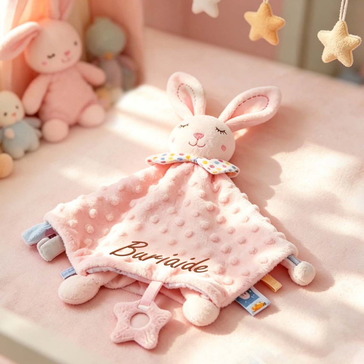Close-up of a pink rabbit lovey with embroidered name and ribbon tags