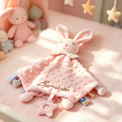 Close-up of a pink rabbit lovey with embroidered name and ribbon tags