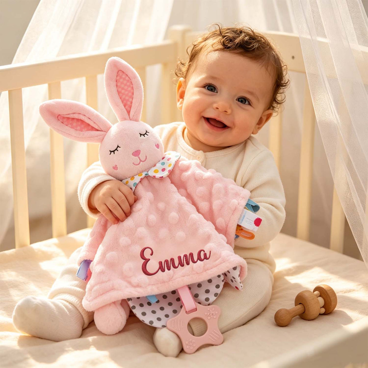 Baby holding a pink embroidered-name rabbit lovey blanket